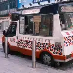 Un camion de glace vintage bleu et blanc garé dans une rue de banlieue déserte sous un ciel crépusculaire