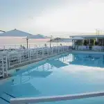 Quatre femmes en peignoir et serviettes dans un spa de luxe, l'une gesticulant dramatiquement