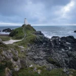 Phare historique en bord de falaise avec sentier et chaussures de randonnée au premier plan