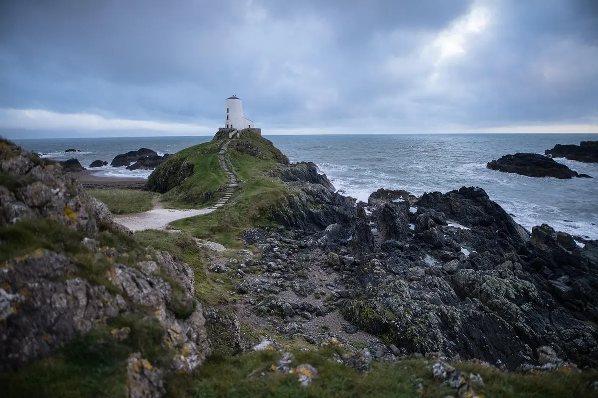 Phare historique en bord de falaise avec sentier et chaussures de randonnée au premier plan